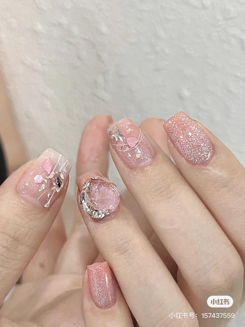 Bộ móng tay được trang trí với màu hồng lấp lánh và các phụ kiện nhỏ, tạo vẻ đẹp tinh tế và sang trọng.