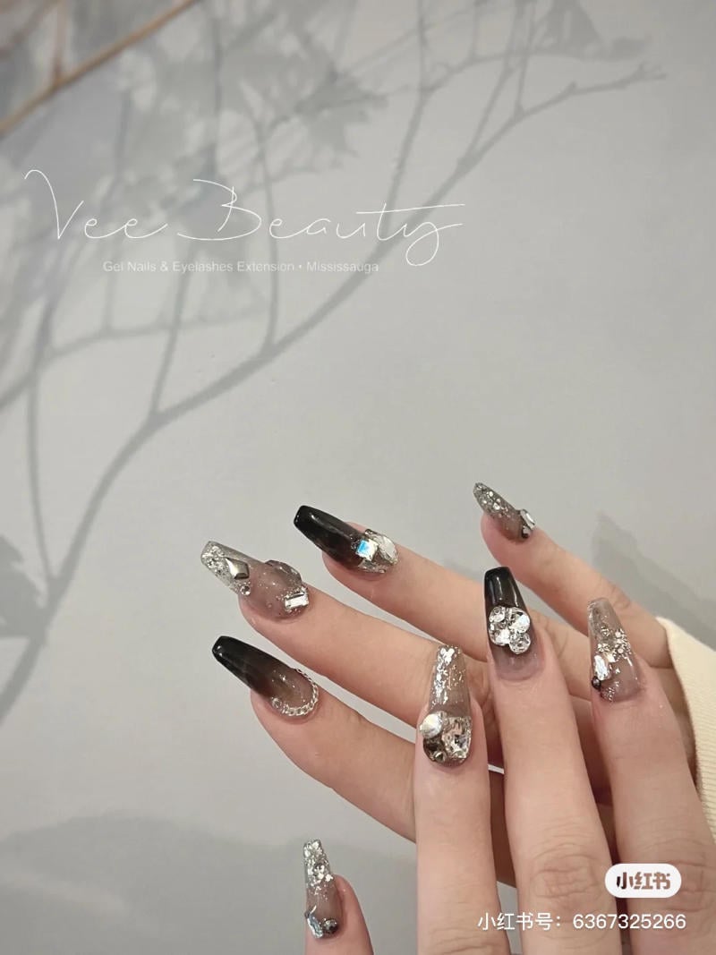 Bàn tay với móng tay dài được trang trí lấp lánh và màu đen, nền trắng có bóng cây mờ ở phía sau.