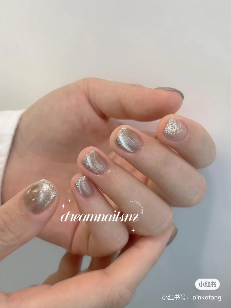 Bàn tay với móng tay được sơn màu bạc lấp lánh, nổi bật trên nền áo trắng.