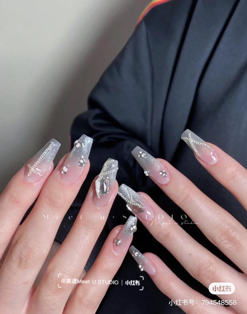 Bàn tay với móng tay giả hình vuông được trang trí bằng kim tuyến bạc và đính đá lấp lánh.