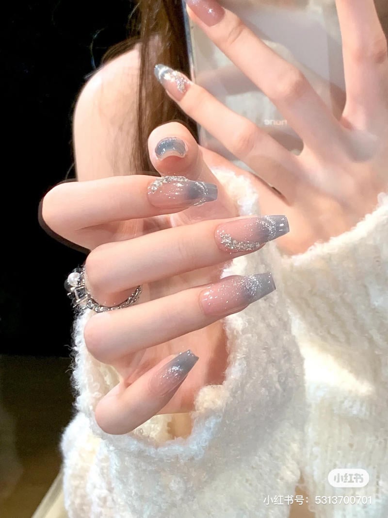 Bàn tay với móng tay được sơn màu ombre xanh bạc, đính kèm kim tuyến, trên nền áo len trắng.