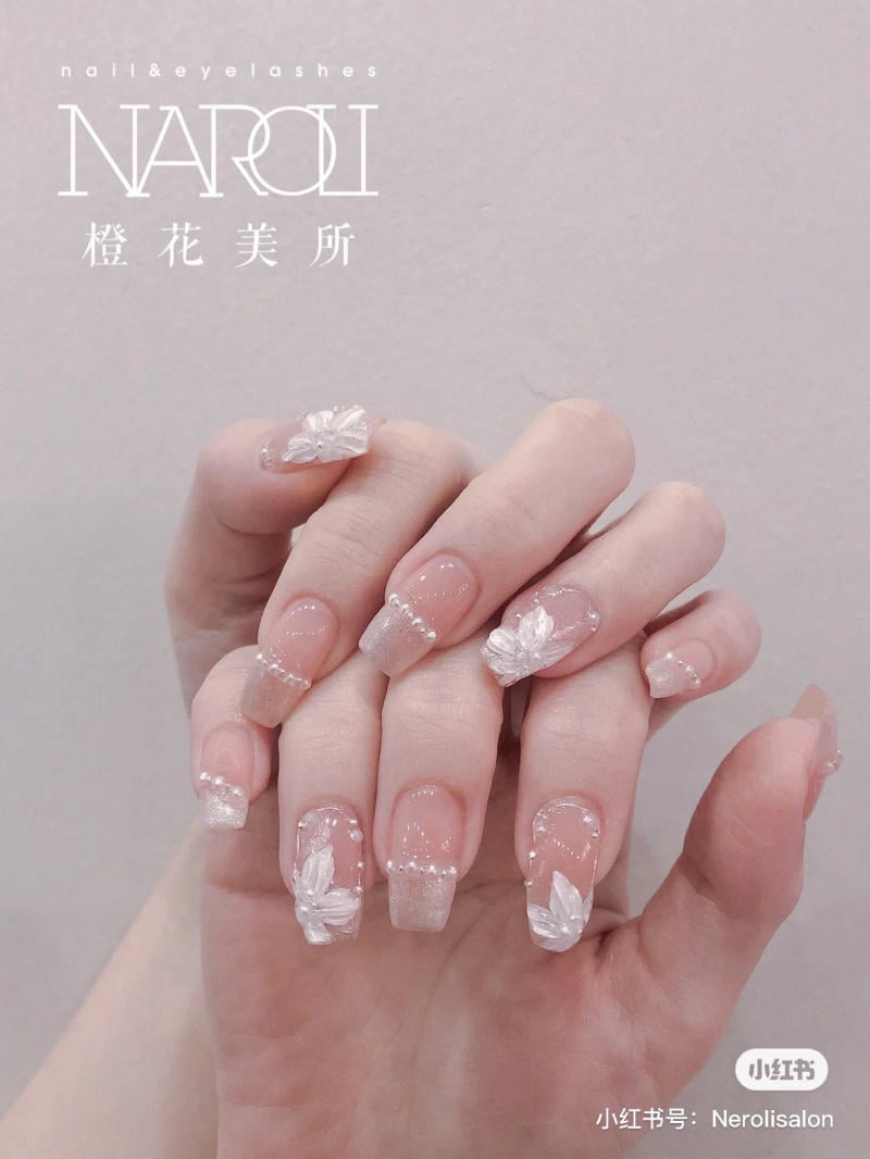 Bàn tay với móng tay được trang trí hoa trắng và đính đá, nền màu hồng nhạt, phong cách nghệ thuật móng tay.