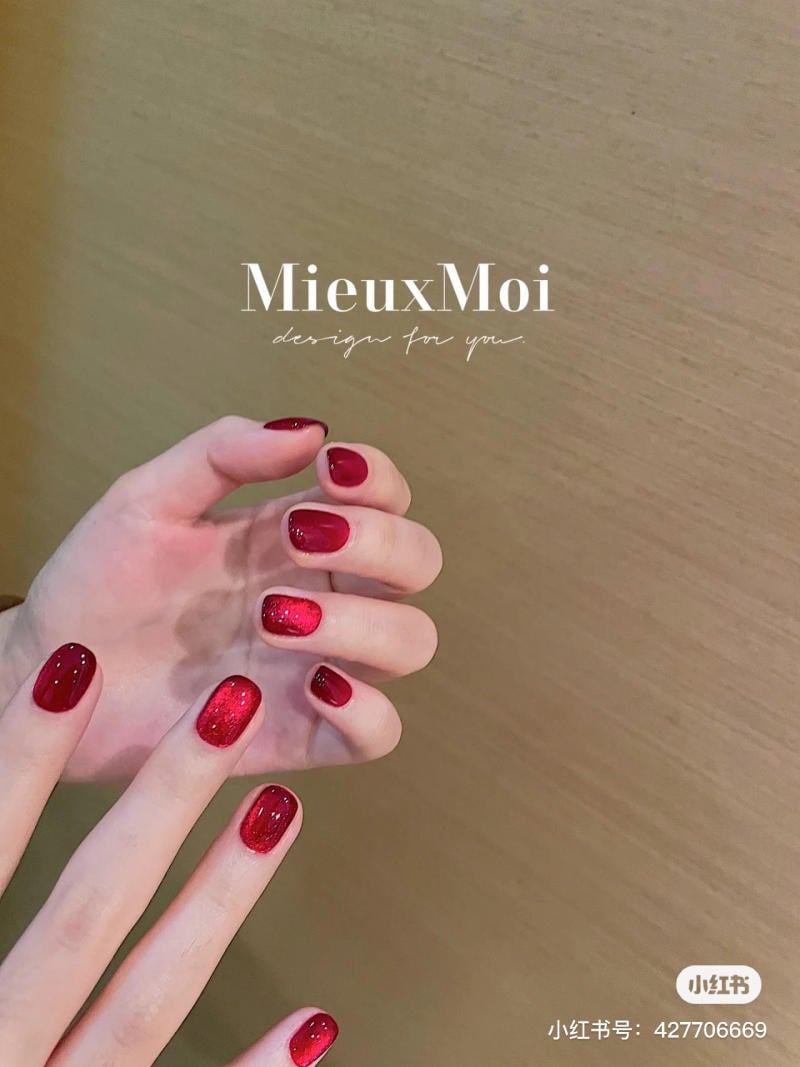 Bàn tay với móng tay sơn màu đỏ lấp lánh, nền màu nâu nhạt.