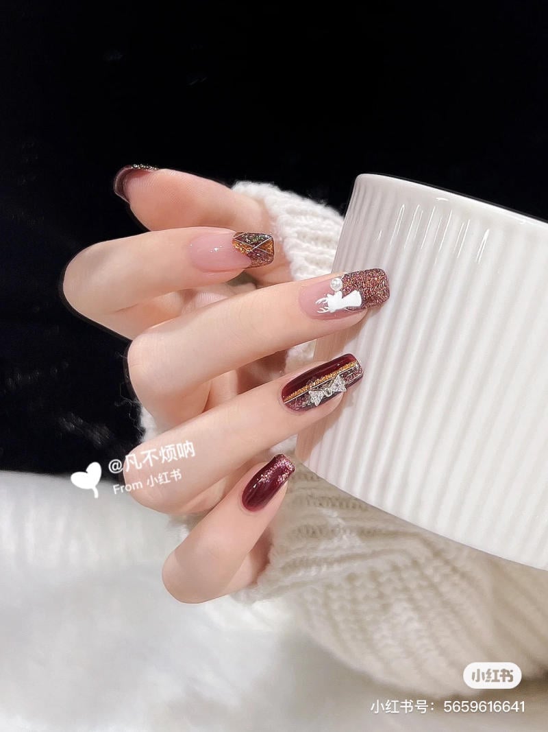 Bàn tay với móng tay sơn đỏ và trang trí họa tiết cầm một chiếc cốc trắng có vân sọc.