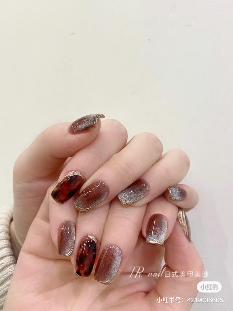Bàn tay với móng tay được trang trí nghệ thuật màu nâu bóng kết hợp hiệu ứng ánh kim nổi bật.