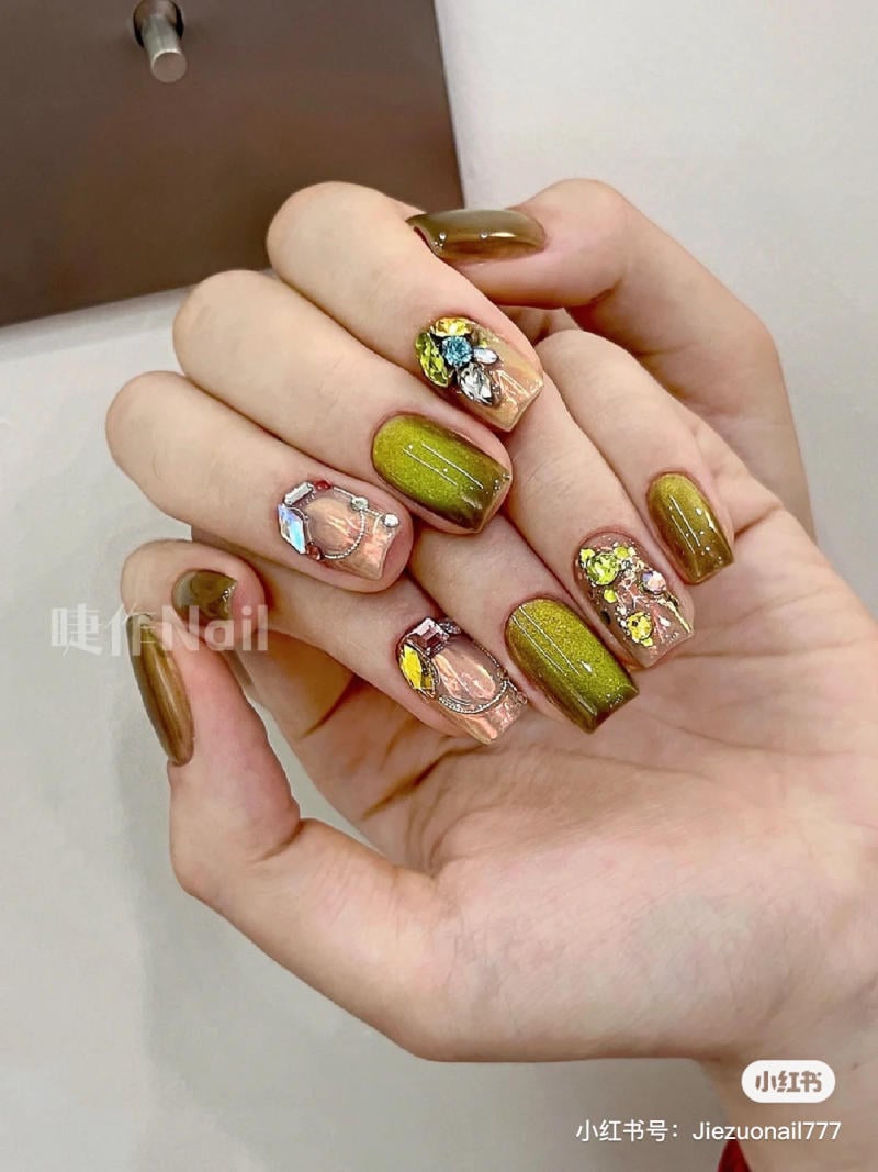 Bàn tay với móng tay được sơn màu xanh lá và trang trí bằng đá lấp lánh.