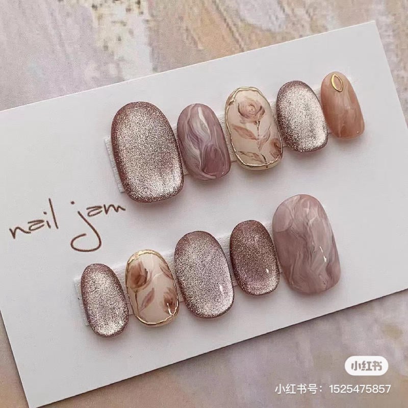 Bộ móng giả với họa tiết cẩm thạch và ánh kim, đặt trên nền giấy trắng có chữ "nail jam".