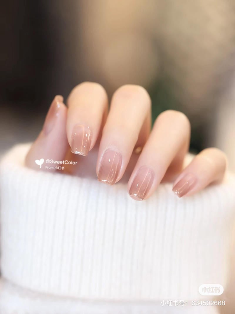 Bàn tay với móng tay được sơn màu hồng nhạt, áo len trắng, phông nền mờ.
