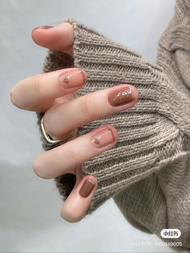Bàn tay với móng tay được sơn màu nâu nhạt và họa tiết, mặc áo len màu nâu nhạt.