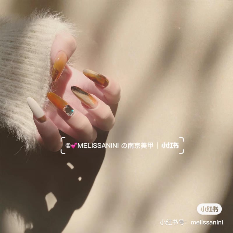 mau-nail-mong-nhon-dai__1__dbf366a4170b4164a0c6019cb81acc46 Bàn tay với móng tay trang trí nghệ thuật, ánh sáng chiếu qua tạo bóng trên nền màu be.