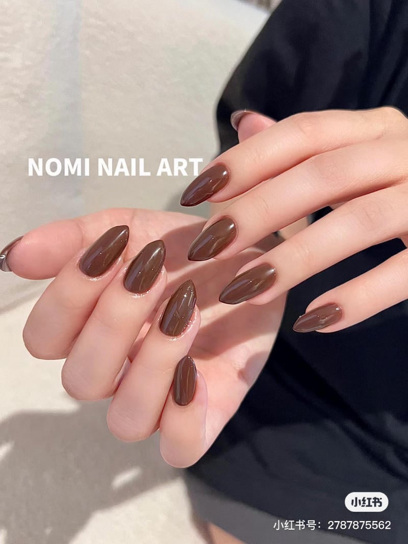 mau-nail-mong-nhon-dai__2__ec162d039cb548e1b090cc33ff60147d Bàn tay với móng được sơn màu nâu bóng, hình dáng nhọn, nền tối giản.