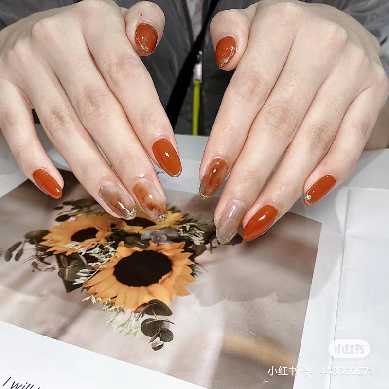 mau-nail-mong-nhon-dai__4__521d3f73002a42888e229ea402d8610f Bàn tay với móng tay màu cam và nâu nghệ thuật trên nền bức ảnh hoa hướng dương.