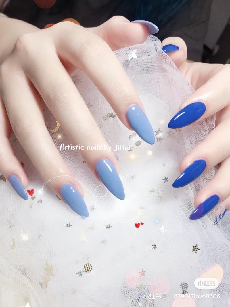 mau-nail-mong-nhon-dai__6__74e028185cd94f7db3b2e9a4b8fbee5d Bàn tay với móng tay dài, sơn màu xanh nhạt và xanh đậm, trên nền vải trắng có họa tiết sao.