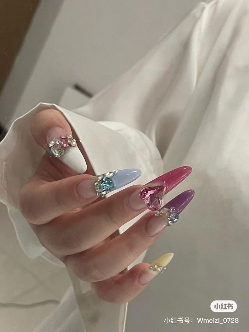 mau-nail-mong-nhon-tron__9__299ea50683d04d598a538e87e235cced Bàn tay với móng tay dài, sơn nhiều màu sắc và trang trí đá quý nổi bật.