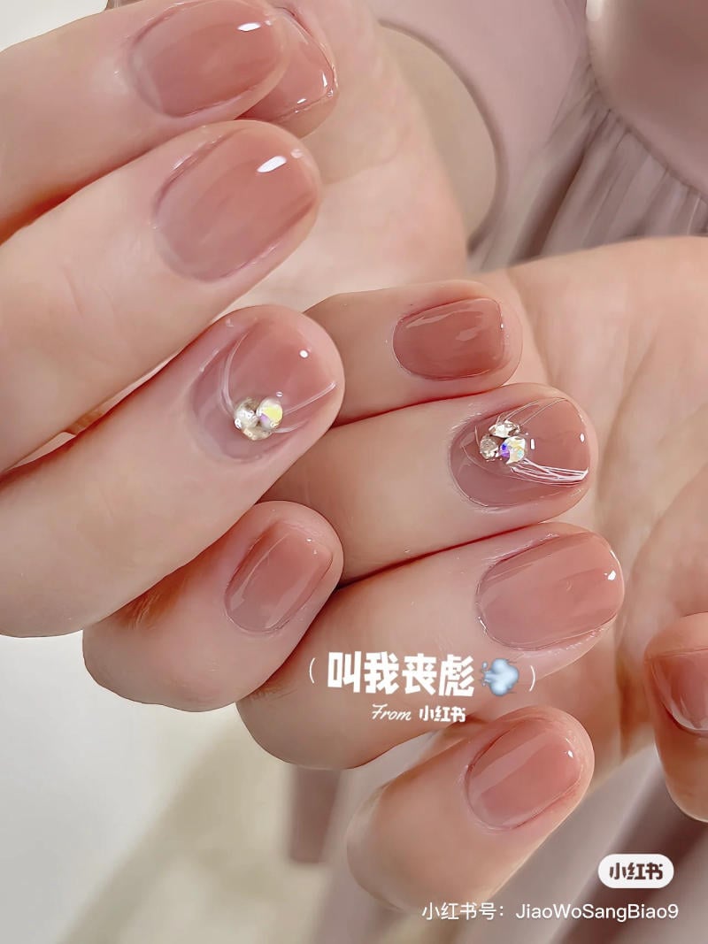 Bàn tay với móng tay màu hồng nhạt, đính đá trang trí nhỏ, chụp cận cảnh, nền màu sáng.