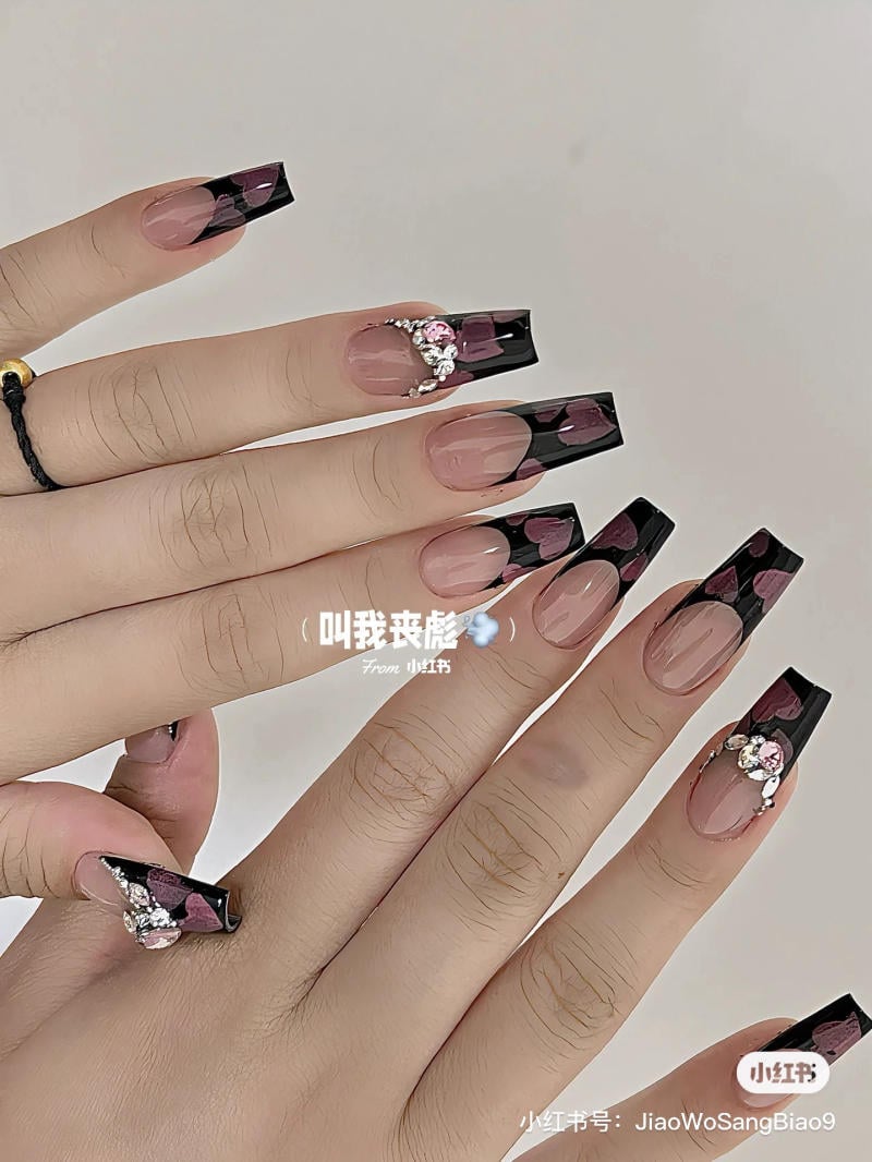 Bàn tay với móng tay dài, thiết kế họa tiết đen và hồng, đính đá trang trí.