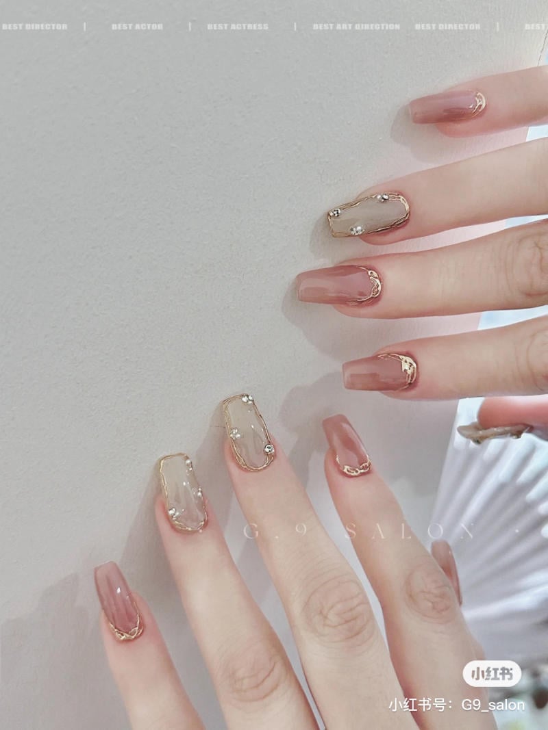 Bàn tay với móng tay được trang trí đẹp mắt, màu sắc nhẹ nhàng, có đính đá và viền vàng tinh tế.