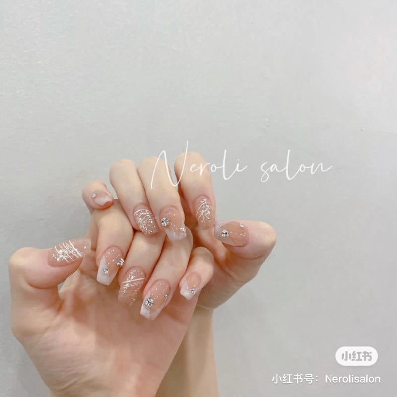 Bàn tay với móng tay được trang trí tinh tế, nền màu nude và họa tiết kim tuyến lấp lánh.