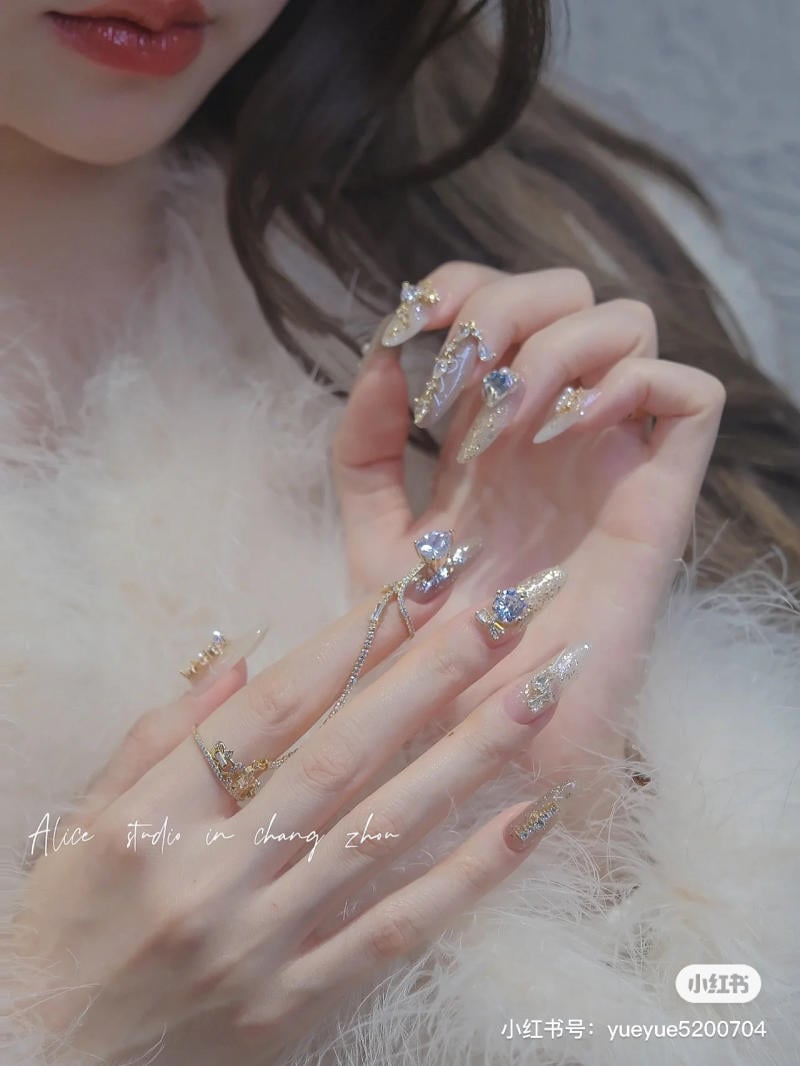 Người mẫu với móng tay dài được trang trí bằng đá lấp lánh và dây trang sức, mặc áo lông mềm mại.