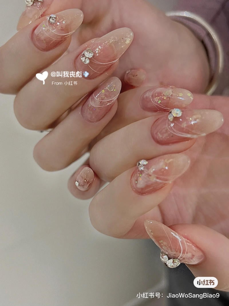 Bàn tay với móng tay được trang trí bằng sơn trong suốt, đính đá và hoa văn tinh xảo.