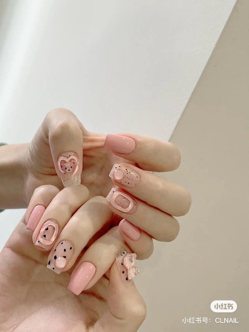 Bàn tay với móng tay sơn màu hồng nhạt, trang trí họa tiết và phụ kiện nhỏ xinh.