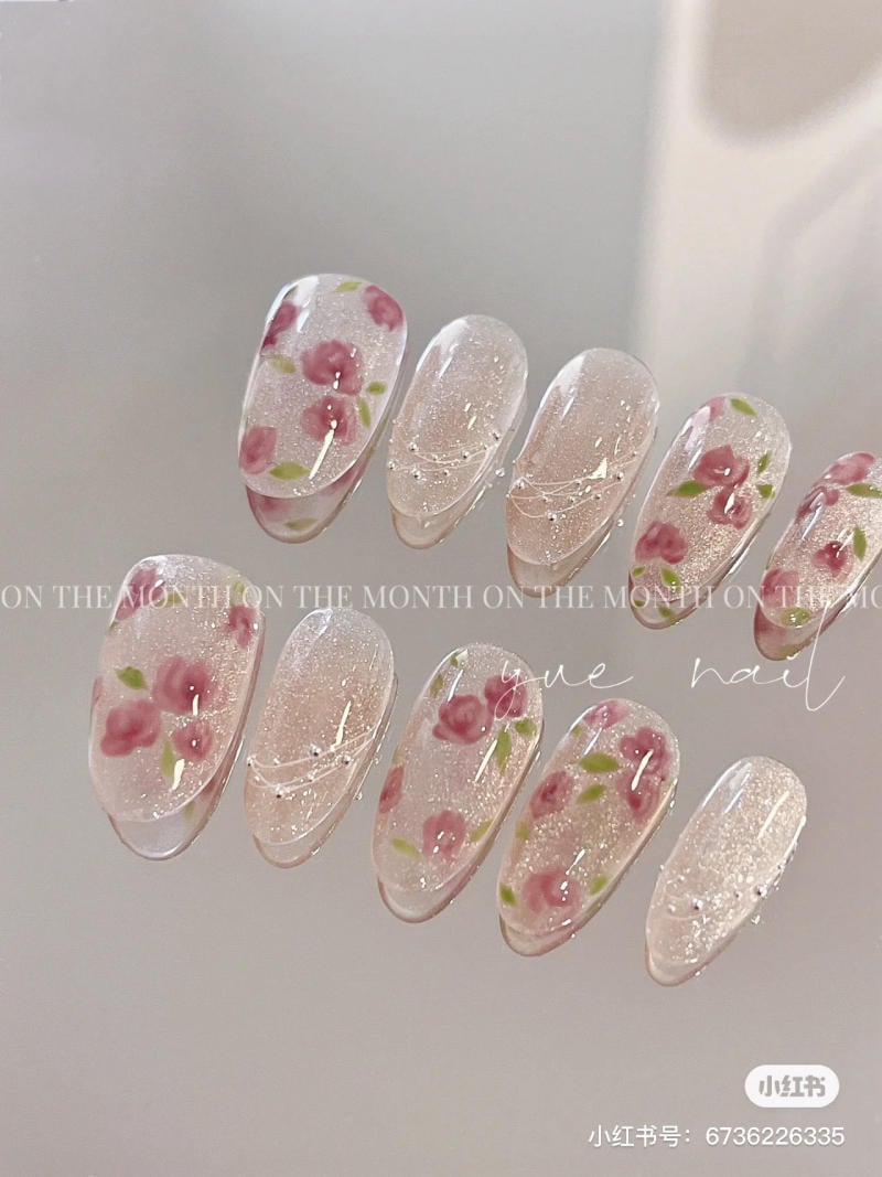 Mẫu móng tay giả màu hồng nhạt, trang trí hoa hồng nhỏ và lấp lánh, xếp trên bề mặt sáng bóng.