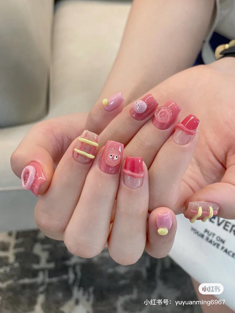 Bàn tay với móng tay được trang trí họa tiết và màu sắc nổi bật, bao gồm hồng và vàng.