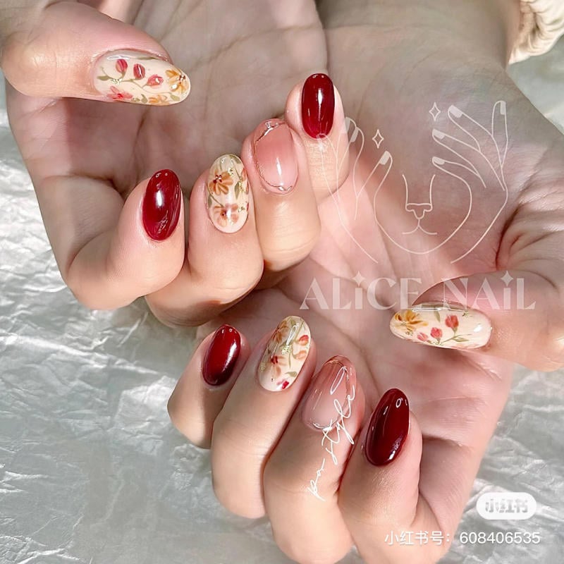 Bàn tay với móng tay được trang trí họa tiết hoa và màu đỏ bóng nổi bật, trên nền giấy bóng.