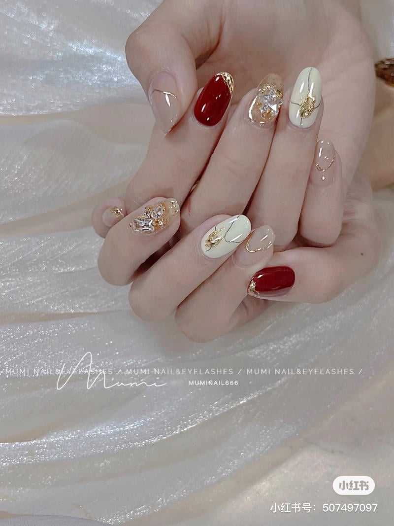 Bàn tay với móng được trang trí cầu kỳ, phối màu đỏ, trắng và họa tiết vàng trên nền vải ánh kim.