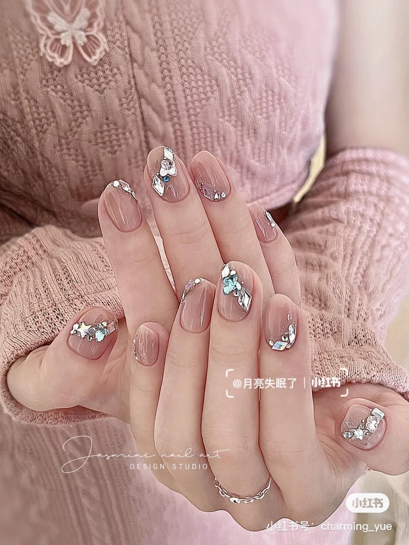 Bàn tay với móng tay được trang trí hoa văn và đá, trên nền áo len hồng có họa tiết.