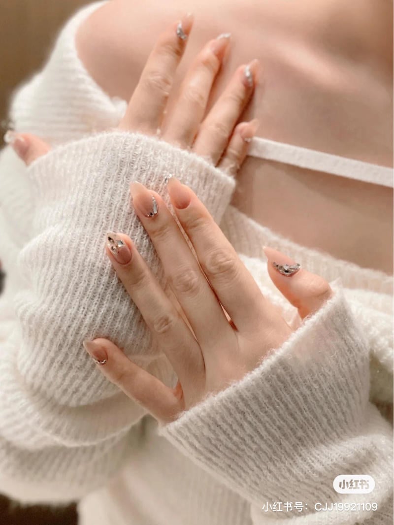 Đôi tay với móng tay trang trí, chạm vào vai, áo len trắng mềm mại.