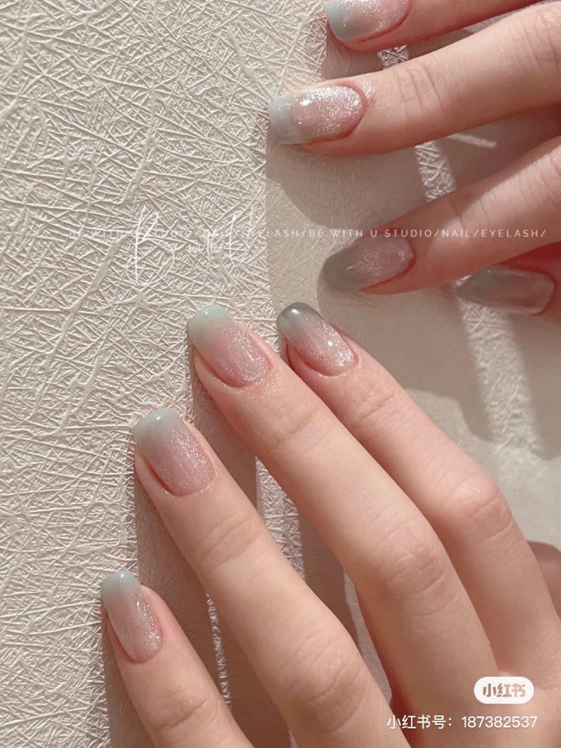 Bàn tay với móng tay sơn màu ombre lấp lánh, đặt trên bề mặt có hoa văn.