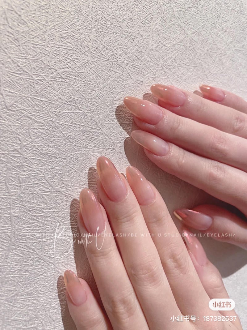 Bàn tay với móng tay được sơn màu hồng nhạt, nền là bề mặt có kết cấu.