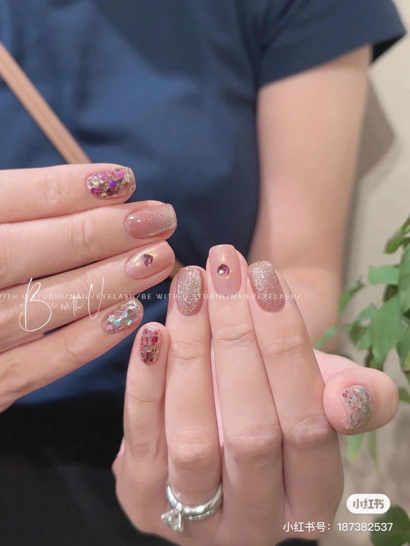 Hai bàn tay với móng được trang trí bằng họa tiết lấp lánh và đính đá, một tay đeo nhẫn bạc.
