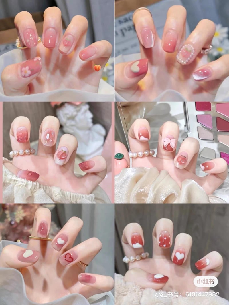 Bàn tay với móng tay được trang trí họa tiết trái tim và hoa trên nền màu hồng và đỏ.