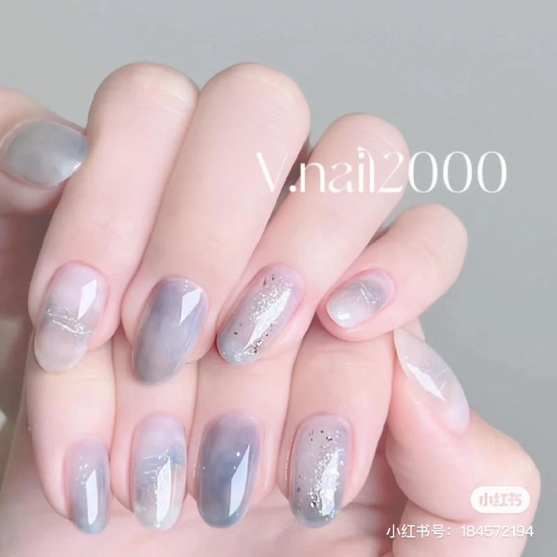 Bàn tay với móng tay được sơn màu xám nhạt, trang trí họa tiết ánh kim lấp lánh trên nền xám ombre.