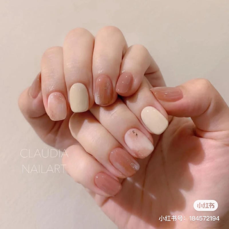 Bàn tay với móng tay được sơn màu nude và hồng, tạo kiểu nghệ thuật đơn giản và thanh lịch.