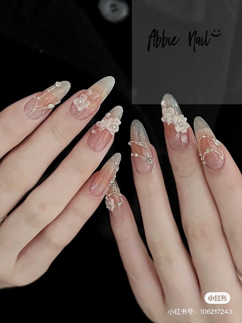 Bàn tay với móng tay dài, thiết kế hoa nổi và kim tuyến tinh tế trên nền trong suốt.