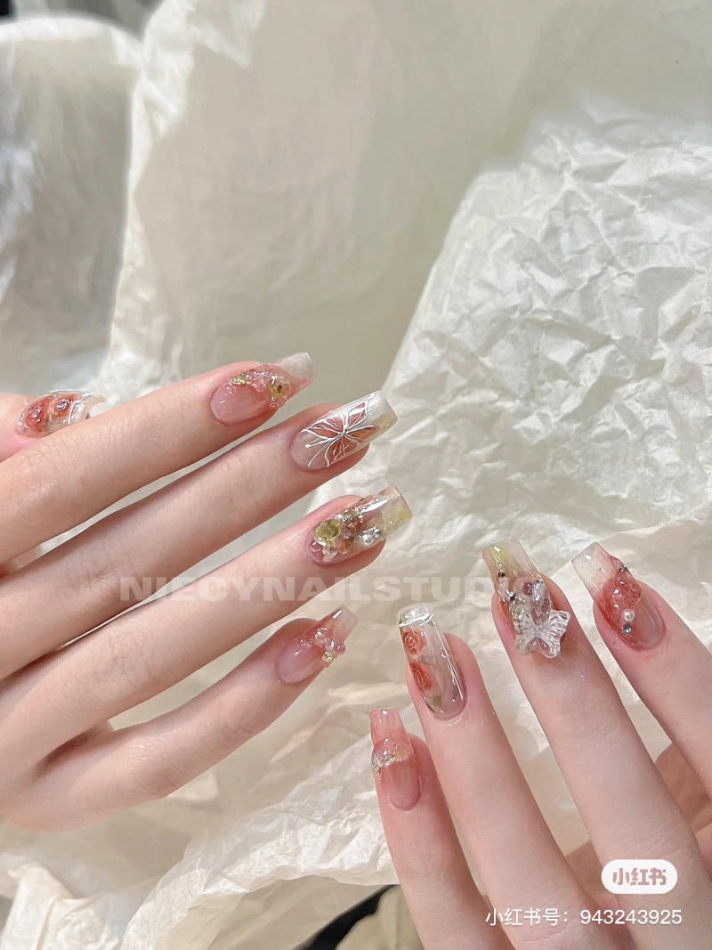 Bàn tay với móng tay dài, được trang trí hoa văn và phụ kiện nổi bật trên nền giấy trắng.