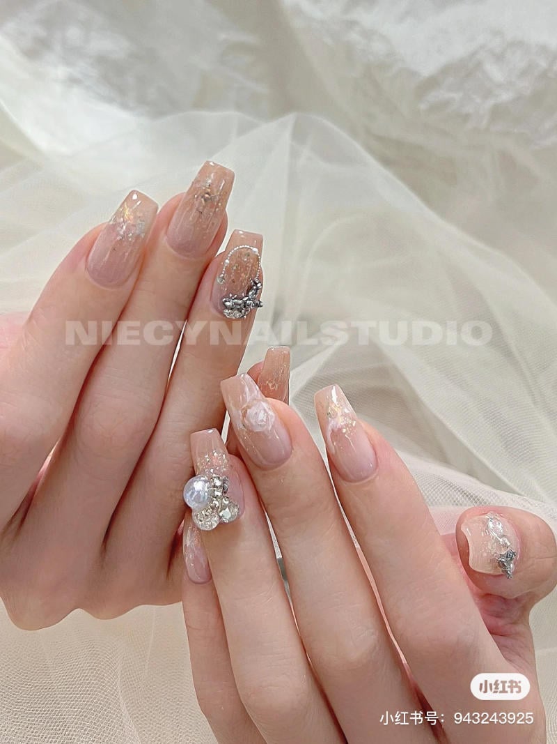 Bàn tay với móng tay được trang trí họa tiết tinh xảo, đính đá lấp lánh trên nền màu nude.