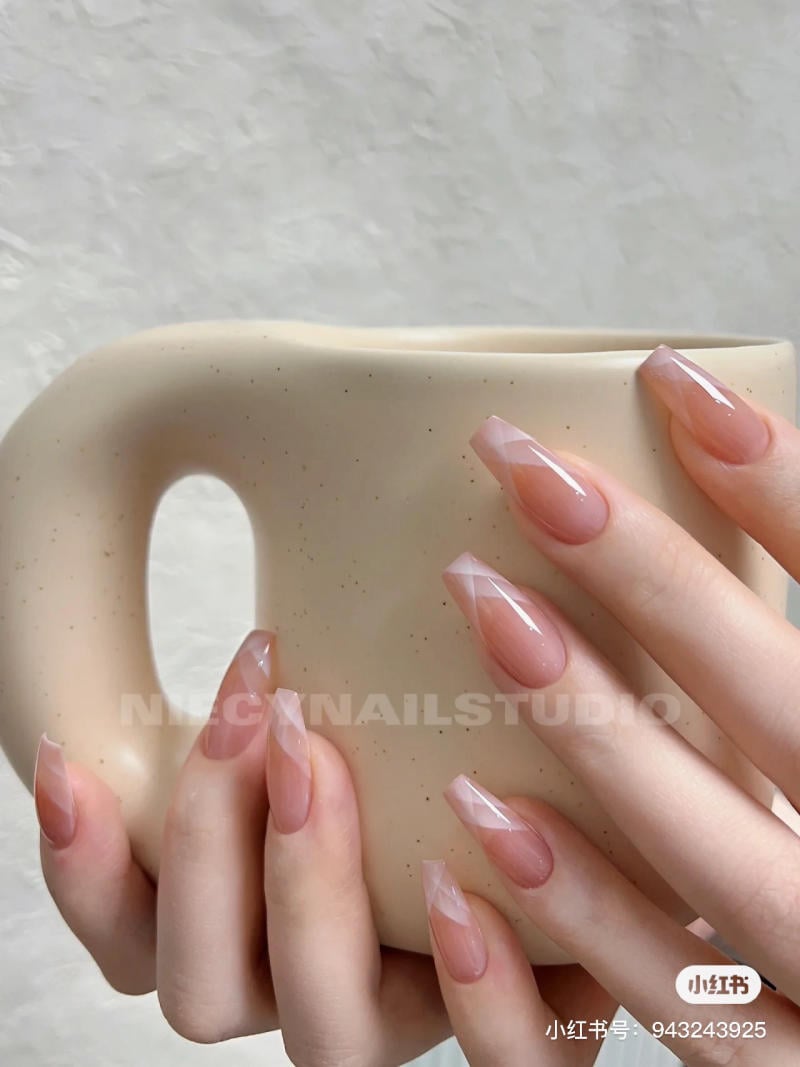 Bàn tay với móng tay được sơn họa tiết, cầm một chiếc cốc màu be, nền trắng đơn giản.