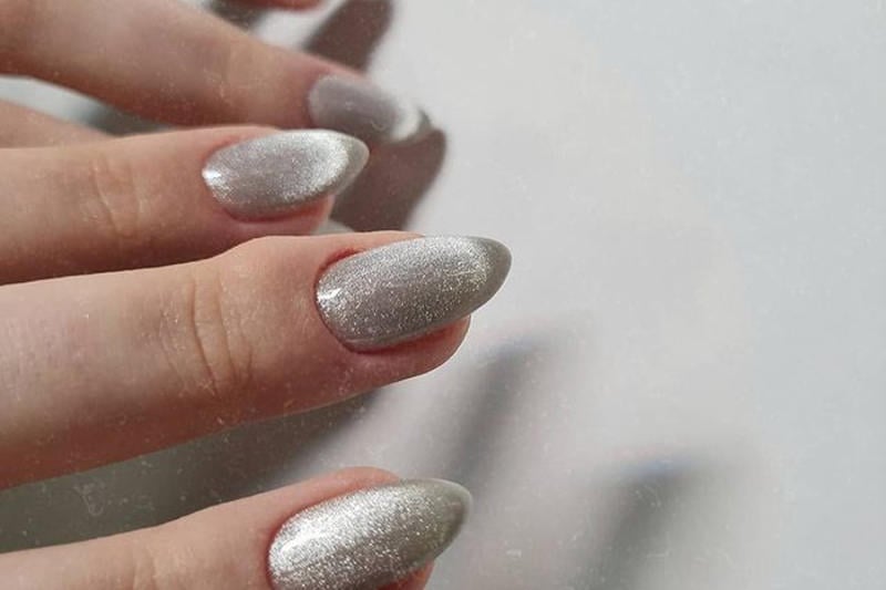 mau-nail-nhu-dep__15__edc6fffd6d204923a7a51be2bc8eb339 Bàn tay với móng tay dài được sơn màu bạc lấp lánh, chụp cận cảnh trên nền màu sáng.