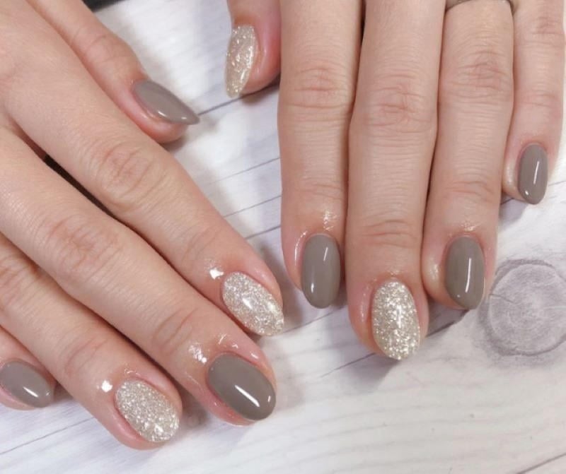mau-nail-nhu-dep__16__4a622762ec2a4f8f9fd416df32c24f81 Bàn tay với móng tay được sơn màu xám và ánh nhũ, trên nền gỗ sáng màu.