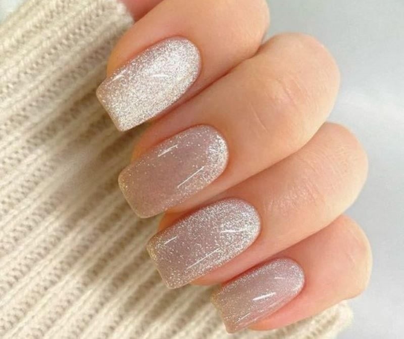 mau-nail-nhu-dep__17__f222a66e13d046a99e052742fc014967 Bàn tay với móng tay sơn màu nhũ bạc lấp lánh, nền là áo len màu sáng.