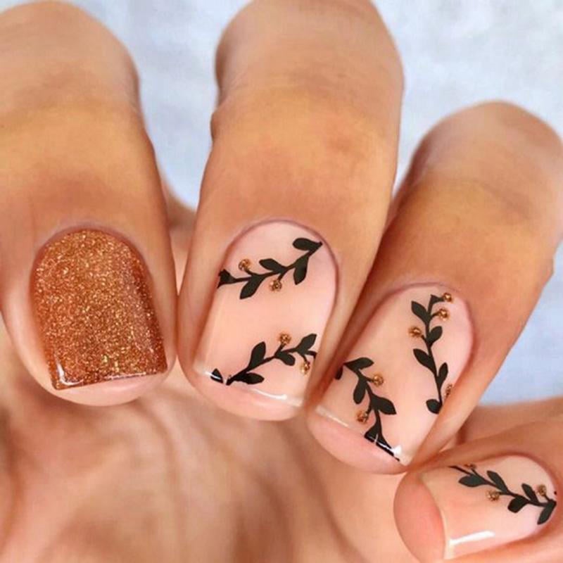 mau-nail-nhu-dep__21__82a6a7ea708a4f98a4222eff19c2a9bc Bàn tay với móng tay trang trí hoa văn lá đen và một móng phủ sơn nâu lấp lánh.