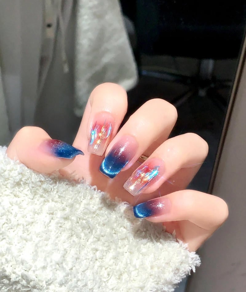 mau-nail-nhu-dep__34__408d11673291455787fe3385f8e74e01 Bàn tay với móng tay dài được sơn màu xanh ombre và trang trí họa tiết lấp lánh, nền là áo lông trắng.
