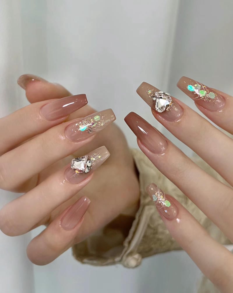 mau-nail-nhu-dep__41__c057335b52074d43ad50960593aa2804 Bàn tay với móng tay dài được sơn màu nâu, trang trí bằng đá và họa tiết lấp lánh.