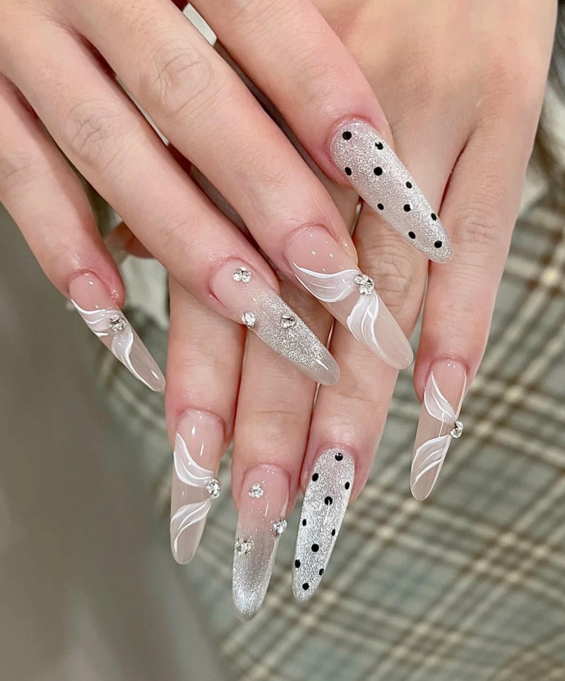 mau-nail-nhu-dep__44__a7820ff836da41329944db0ef8960ec4 Bàn tay với móng tay dài, trang trí họa tiết trắng, đen và bạc, có đính đá lấp lánh trên nền váy kẻ caro.
