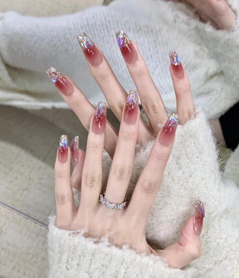 mau-nail-nhu-dep__49__68c49250cf79436b8f73b62d63bfe79e Bàn tay với móng tay dài, sơn màu đỏ ombre, đính kim tuyến lấp lánh, đeo nhẫn kim loại sáng bóng.