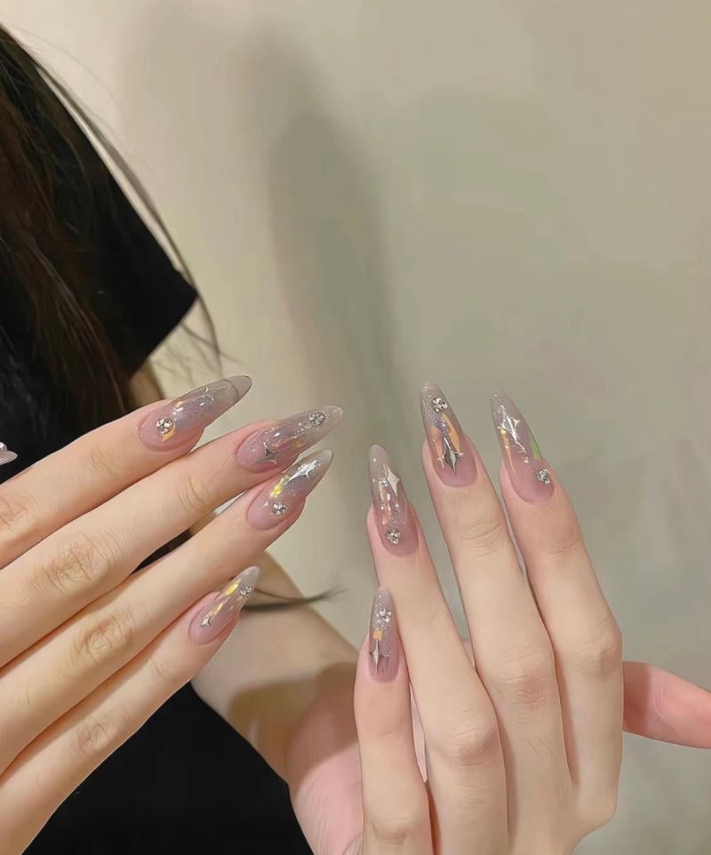 mau-nail-nhu-dep__51__cdfe3d1db71b4f4baa0fe479cbdde3af Bàn tay với móng tay dài được sơn màu hồng nhạt, trang trí họa tiết lấp lánh và đính đá.